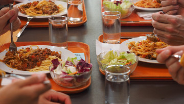 Photo d'une table de cantine avec des plateaux remplis et des mains d'adolescents